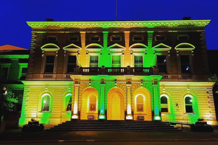An older sandstone building is lit up with green and gold lights.