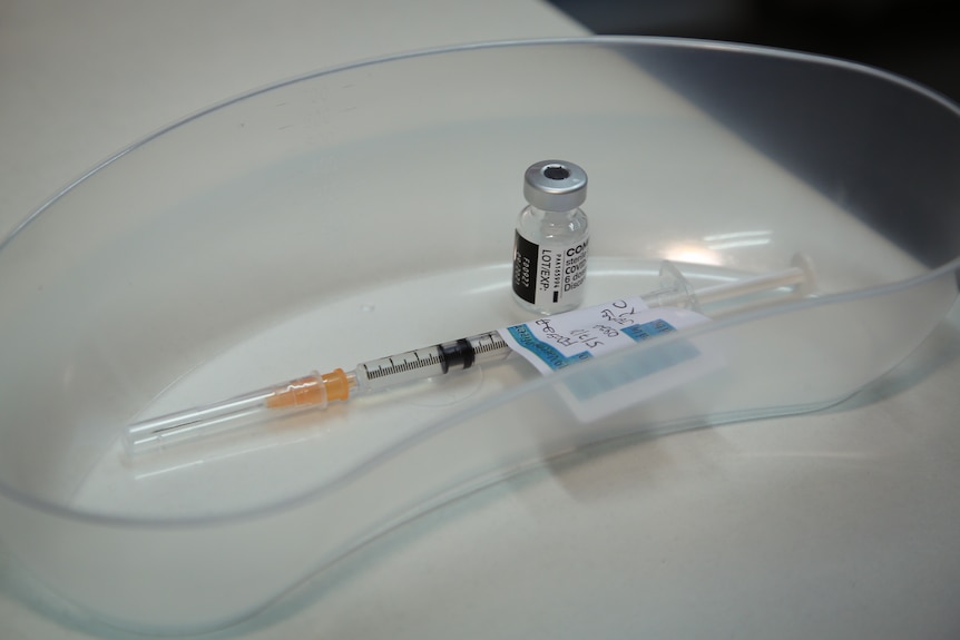 A needle and a Pfizer COVID-19 vaccination in a clear dish.