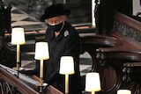 Wearing all black and a face mask, the Queen stands alone in the pews