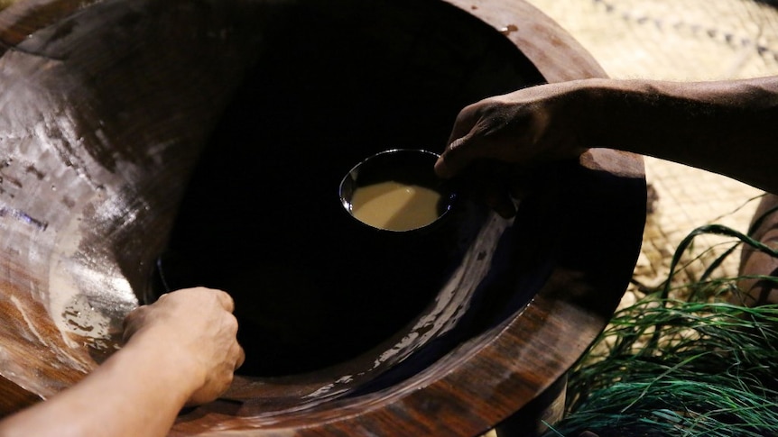 A close up of a hand ladelling out a small cup of kava.