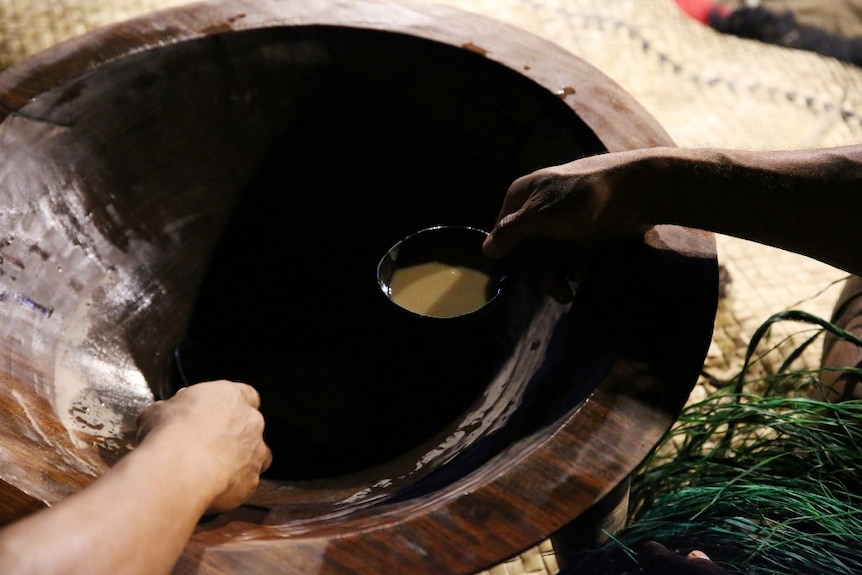 A close up of a hand ladelling out a small cup of kava.