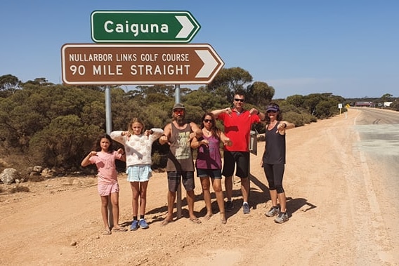 A group of people standing next to a road sign on the Nullarbor.