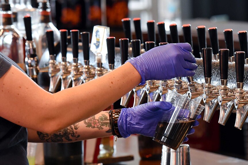 A worker wearing gloves pours drinks in a bar