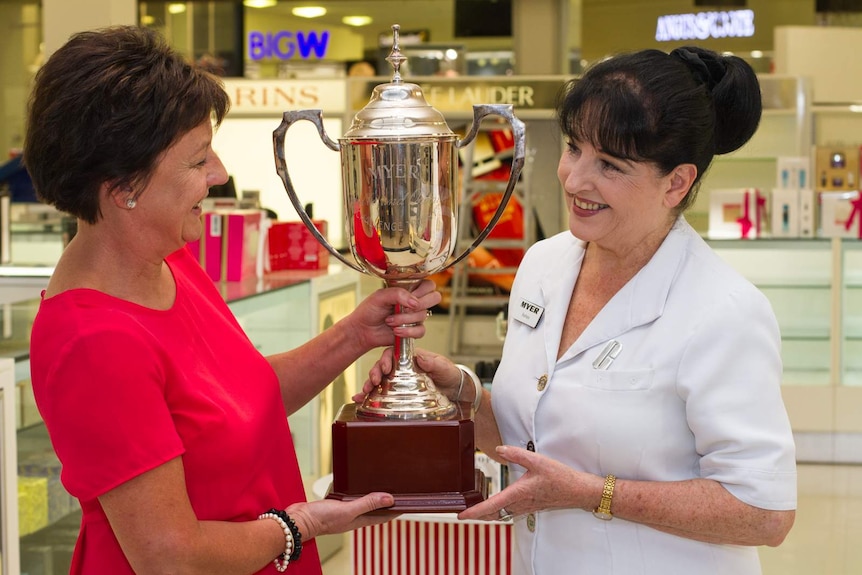 Two women one with a Myer badge on, holding up a big silver trophy