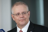 Morrison is looking left to right with some side-eye, lips pursed, and wearing a suit with Australian flag pin.