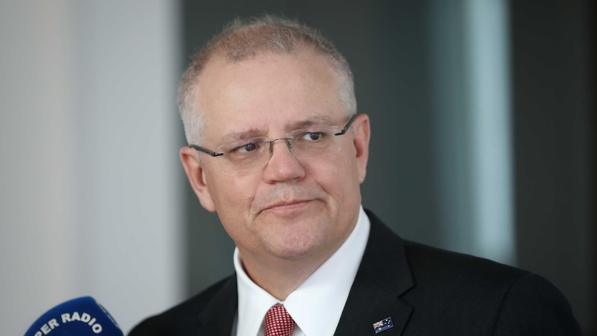 Morrison is looking left to right with some side-eye, lips pursed, and wearing a suit with Australian flag pin.