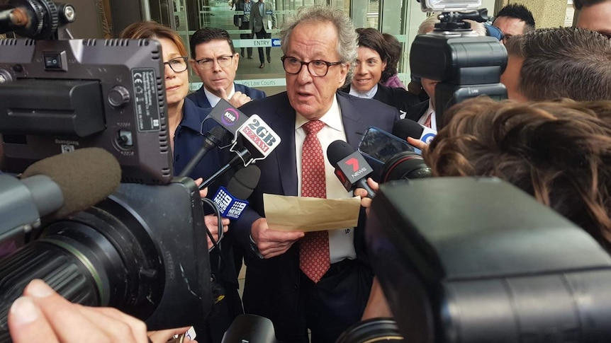geoffrey rush surrounded by microphones and cameras