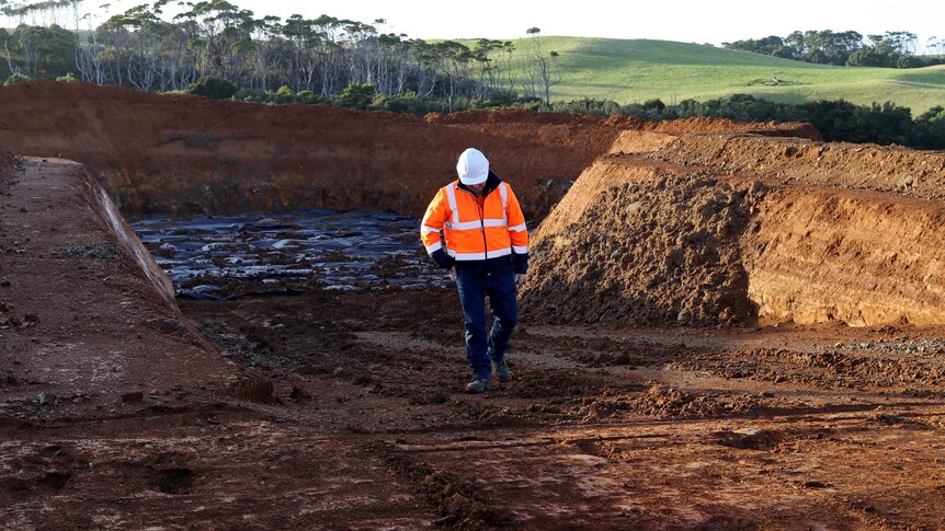 Man in hi vis emerges from a huge pit that will be the foundation of a 200m tall wind turbine