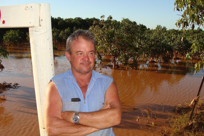 A man in a blue shirt leans on a pole in front of a brown flooded river
