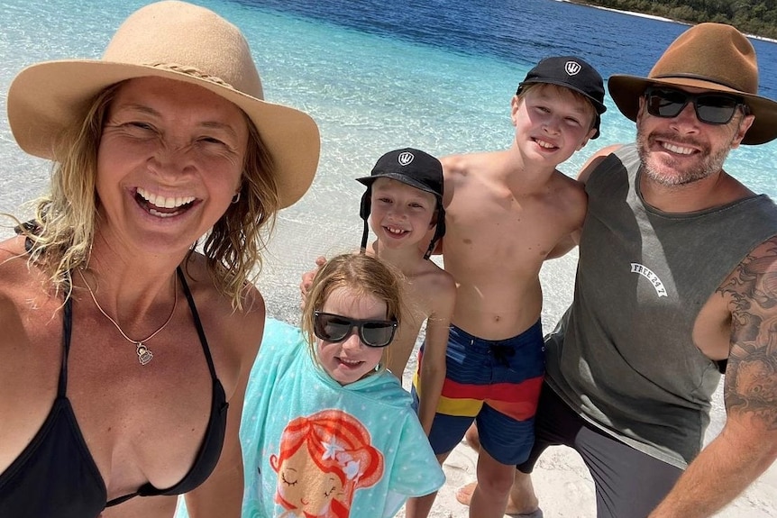 Man and woman with three children posing for a photo on a beach.