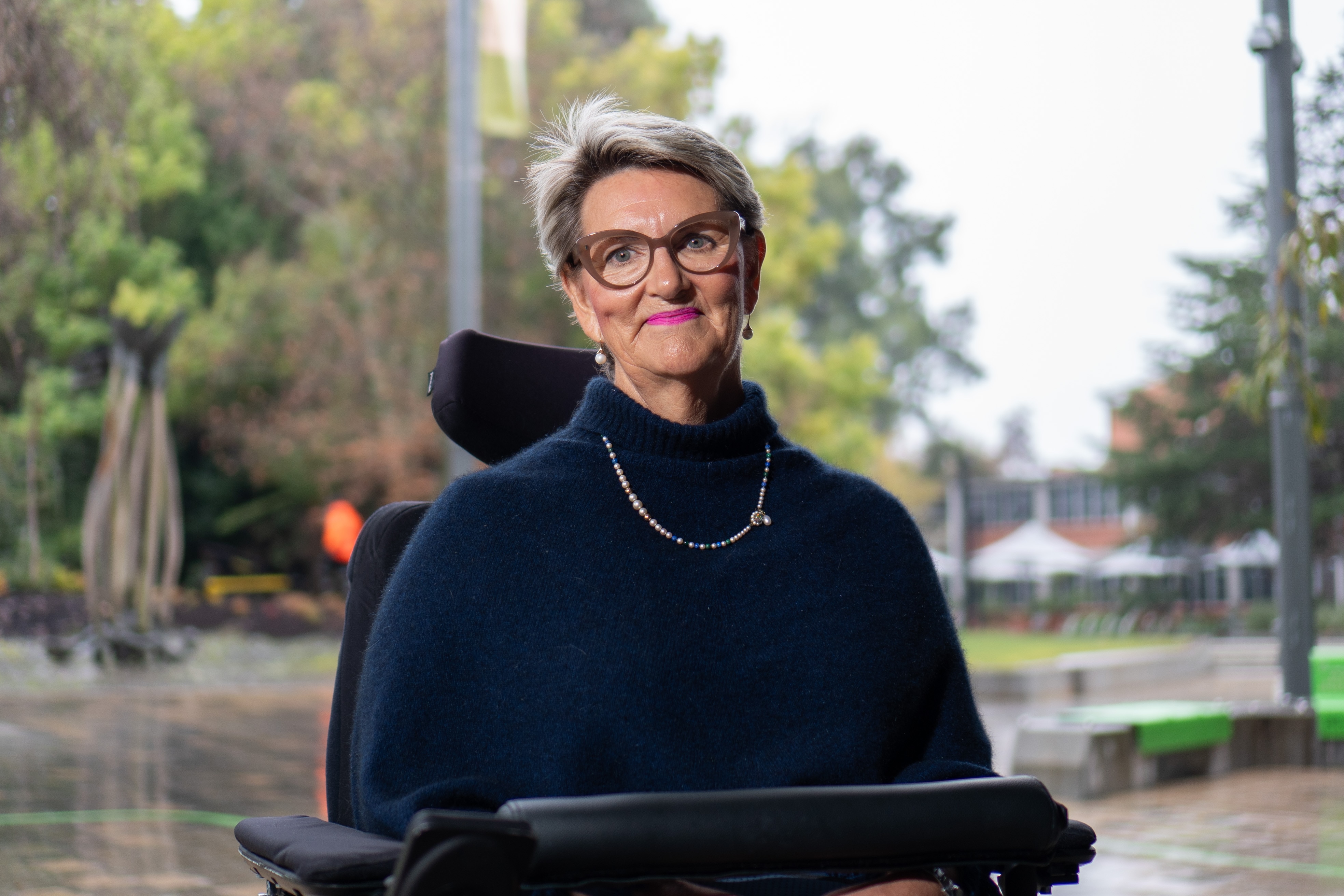 Jane Wardlaw, who is in a wheelchair, in a town square with trees behind her.