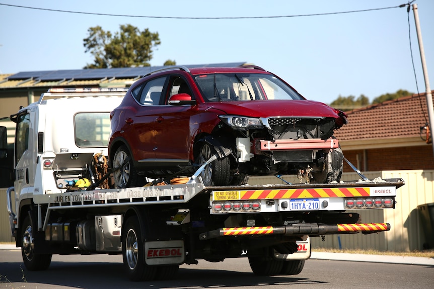 A red SUV on the back of a tow truck being driven through a suburban area.