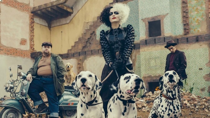 A woman with black and white hair and a leather jacket holds three dalmatians on a leash while two men scowl behind her.