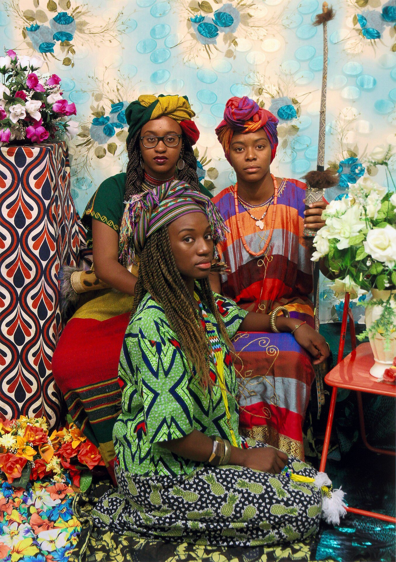 Three African women look expectantly into the camera. Two are sitting on chairs, while a second kneels in front of them