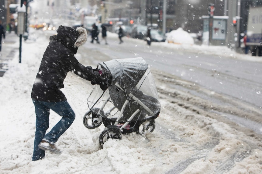A young woman pushes a baby stroller through wet snow on a city street on a snowy day.