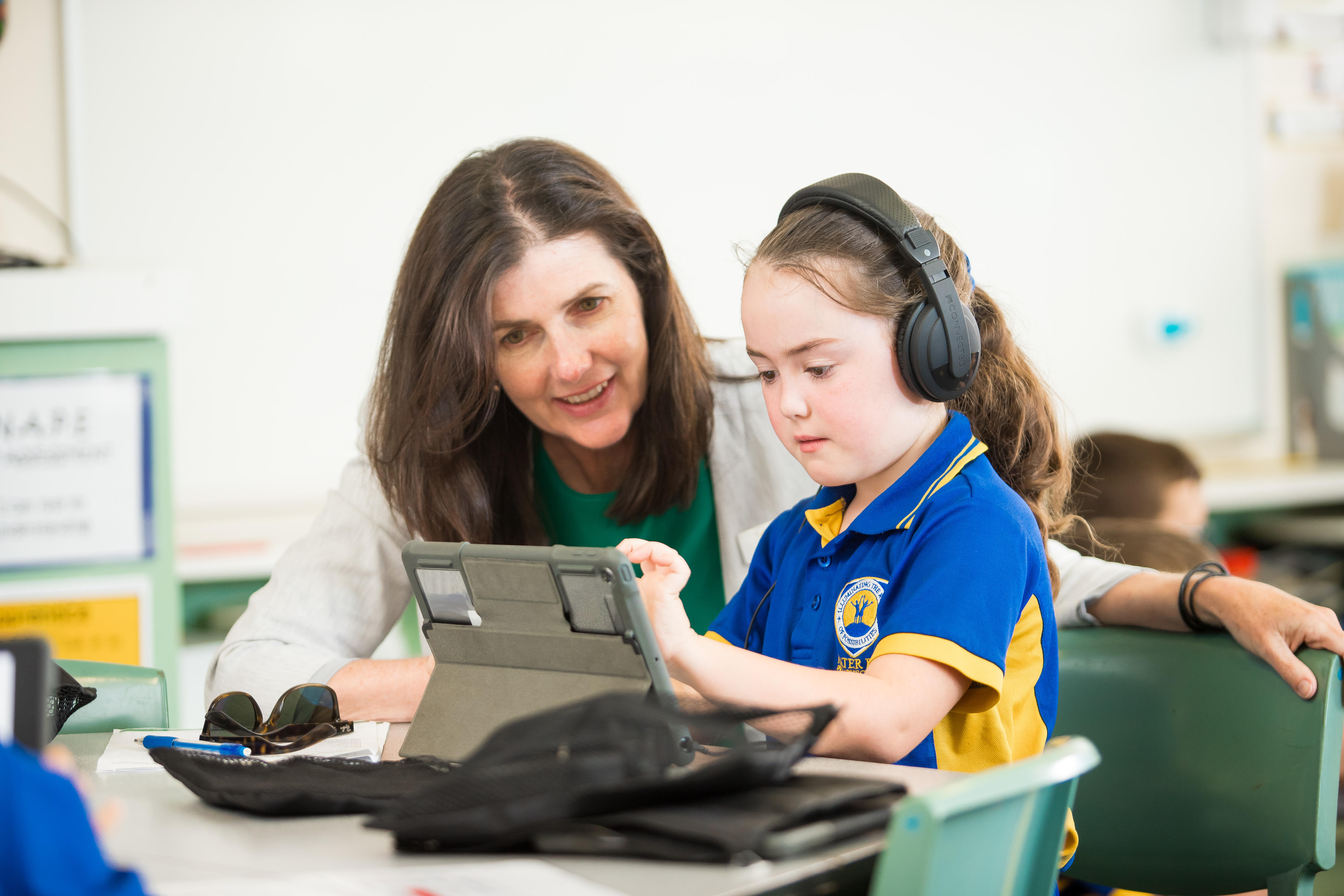 Female teacher looks over the shoulder of a young student using an ipad.