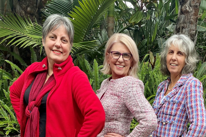 Three women posing for a photo in a garden with hands on hips and smiling.