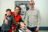 Photo of Adania Evans (centre) with family in front of artwork.