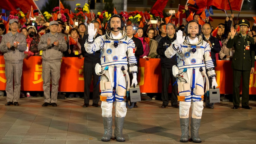 Chinese astronauts Jing Haipeng and Chen Dong wear their space suits and wave before the launch of Shenzhou