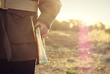 Photo of man dressed in khaki holding a bugle with the sun setting behind him