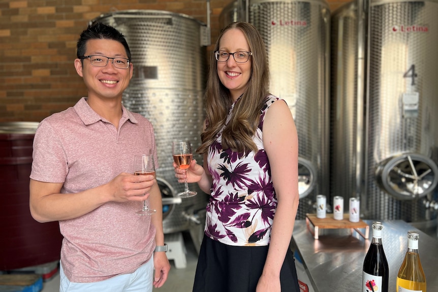 A man and a woman smiles while holding full wine glasses.