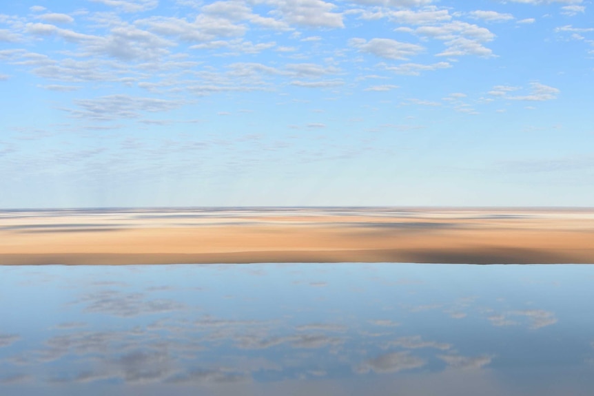 Clouds reflect off a water.  There is a large sand patch in the middle.