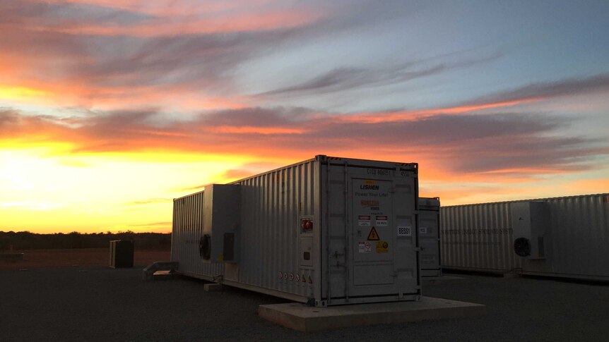 A giant solar battery sits on the ground at sunset.