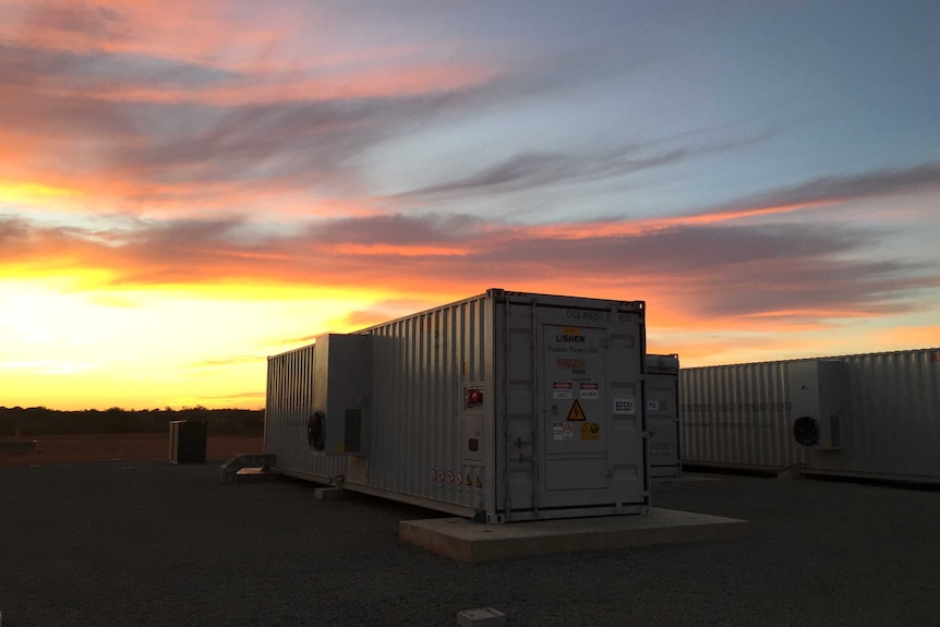 A giant solar battery sits on the ground at sunset.