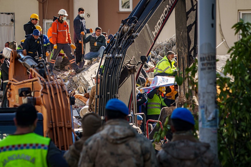 A digger near a group of people at a rubble site