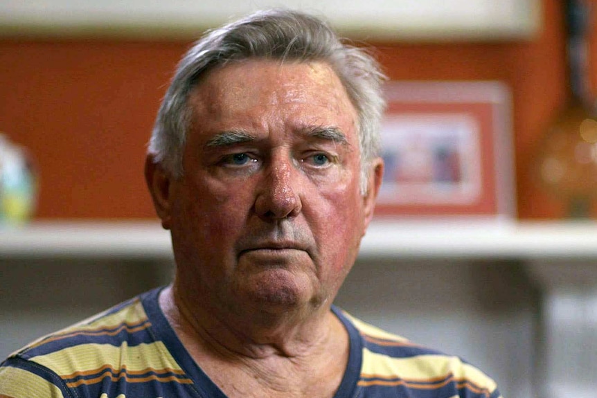 Head shot of Chris Harpur in a yellow, orange and blue striped shirt with a white fireplace and orange wall in the background