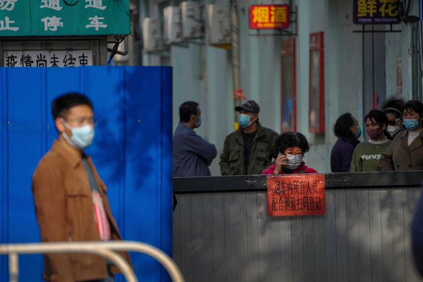 在北京，戴着口罩的中国公民站在障碍物的两侧，一名女子正在打电话。