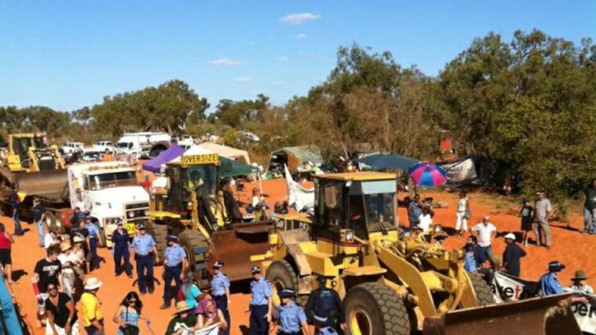 A line of police stand in front of bulldozers and other heavy machinery