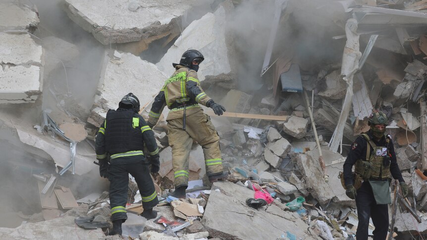 An image of people walking on rubble looking for survivors, there is dust in the air.