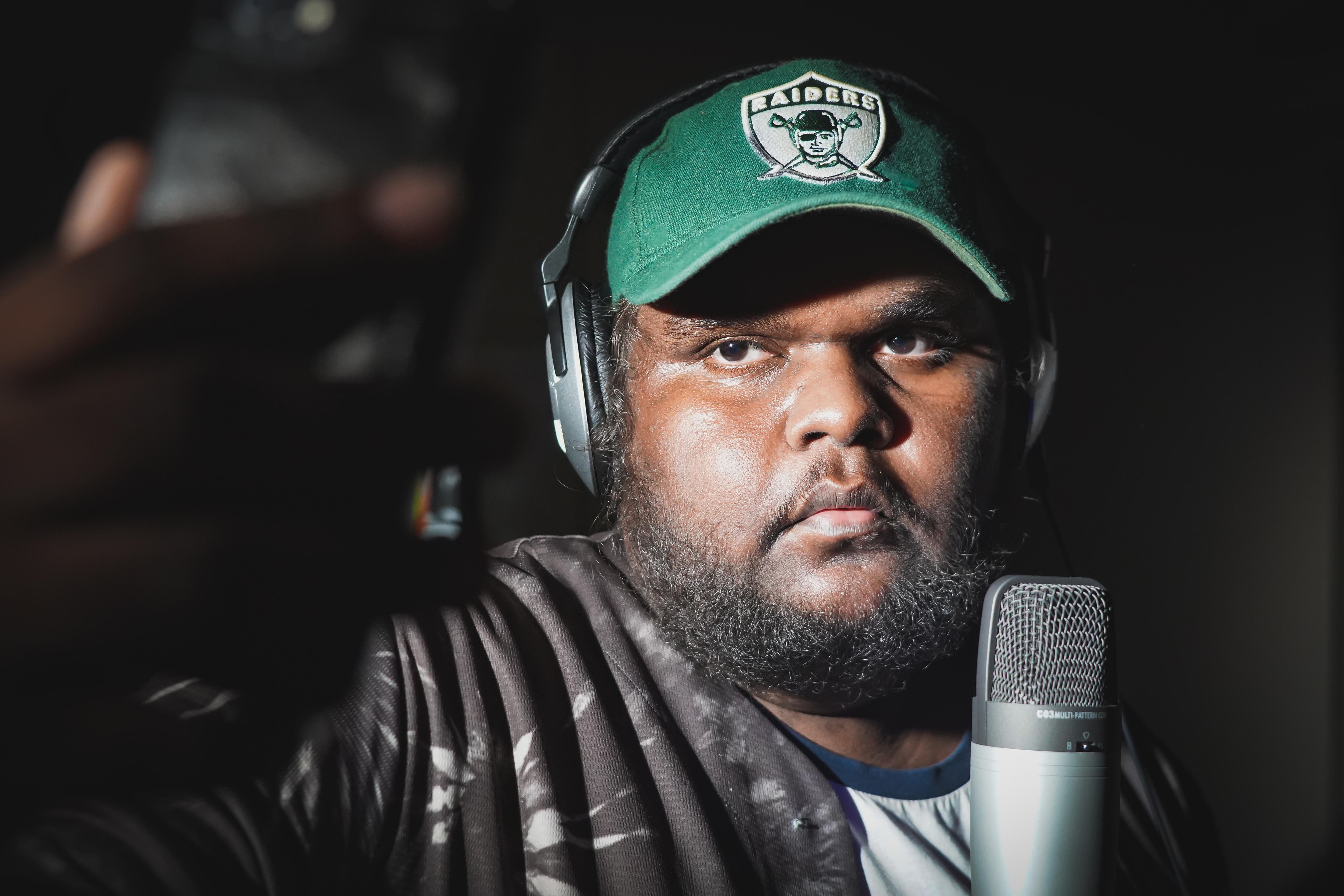 A teen boy in a dark room in front of a microphone wearing a green cap