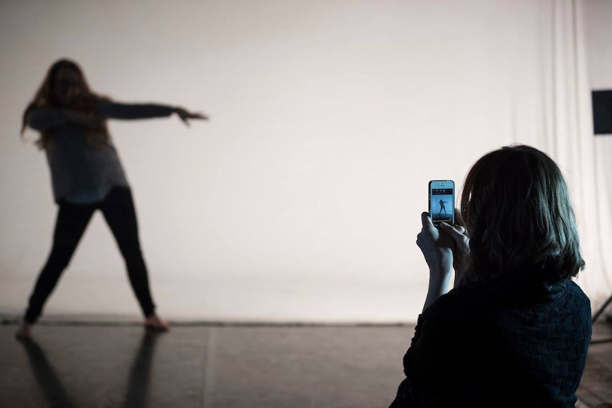 A woman uses a smartphone to capture a gif of a dancing figure.