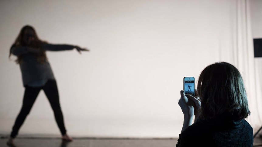 A woman uses a smartphone to capture a gif of a dancing figure.