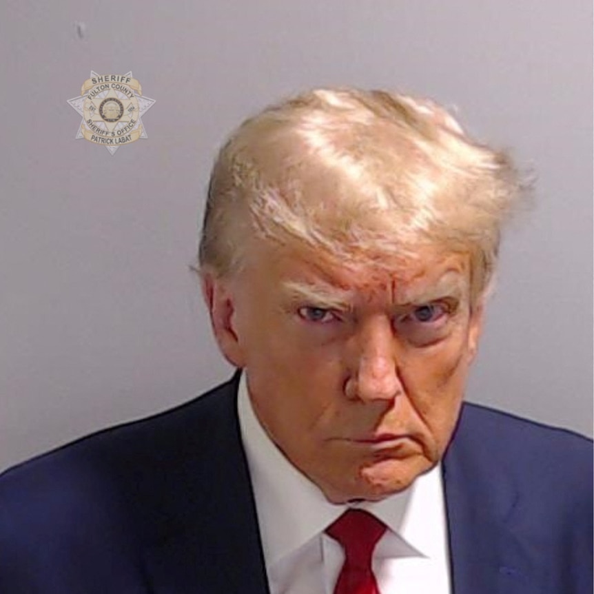 Donald Trump frowns in a mugshot, wearing a suit and red tie