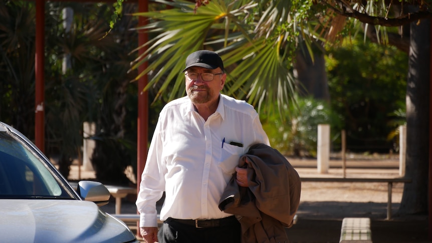 Man walking out of taxi with black hat and white shirt carrying jacket on arm