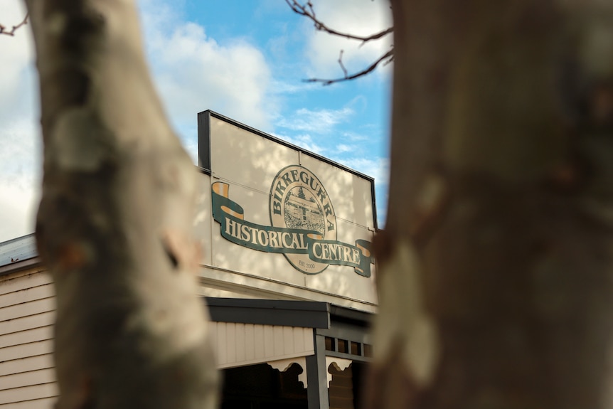 A light-dappled sign for the Birregurra Historical Sign with blue sky in background of building