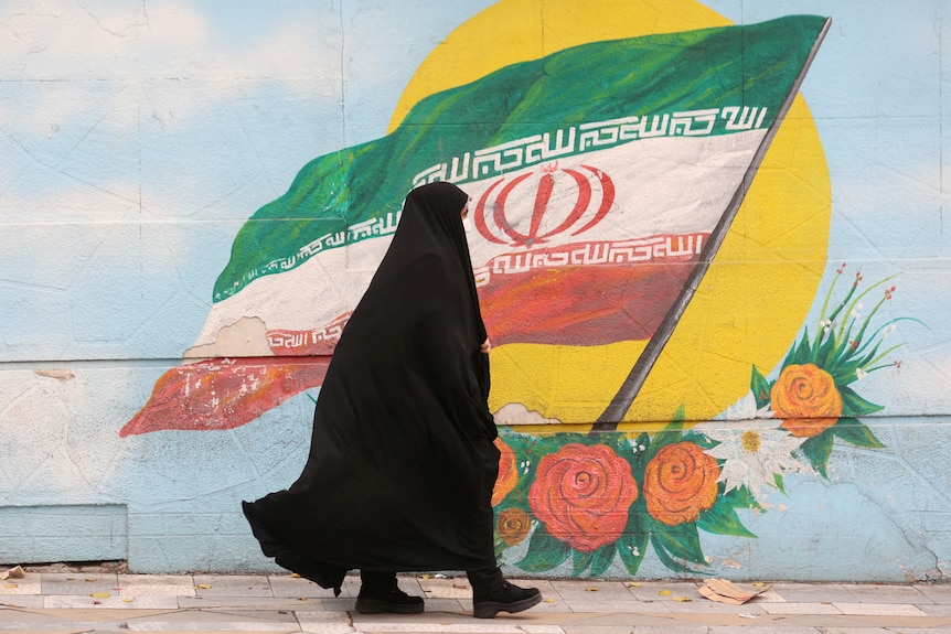 A woman wearing a white cap and an Iranian flag covering her face looks upwards