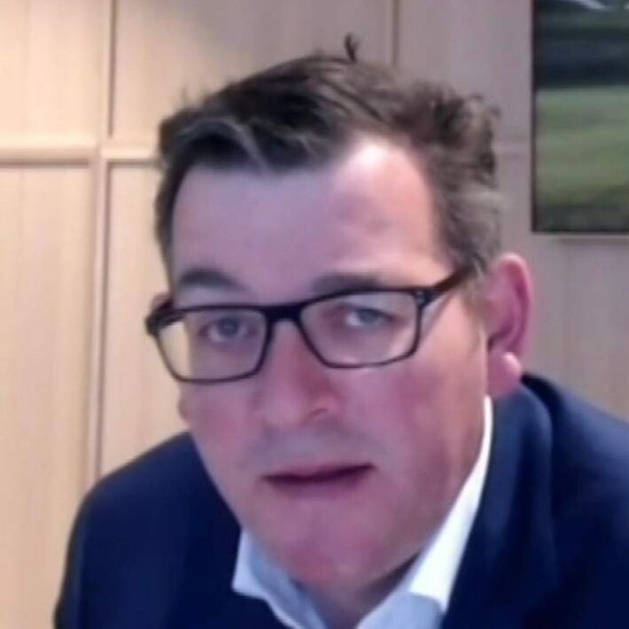 Daniel Andrews sitting at a computer in a room with a screen over his right shoulder.