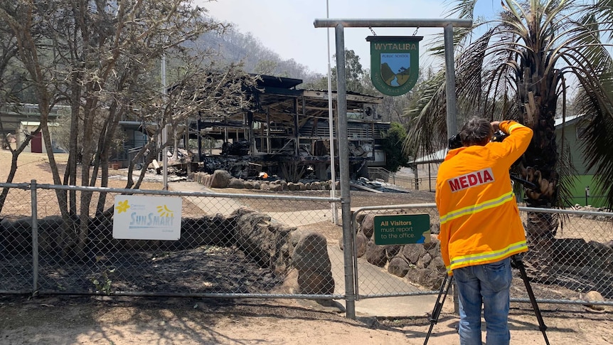 Cameraman wearing protective fire clothing filming burnt out ruins of school.