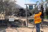 Cameraman wearing protective fire clothing filming burnt out ruins of school.