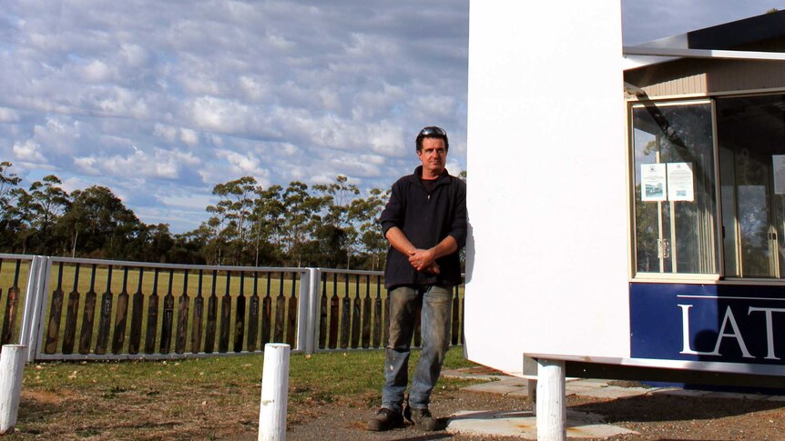 A man standing next to a giant cricket bat in front of an oval