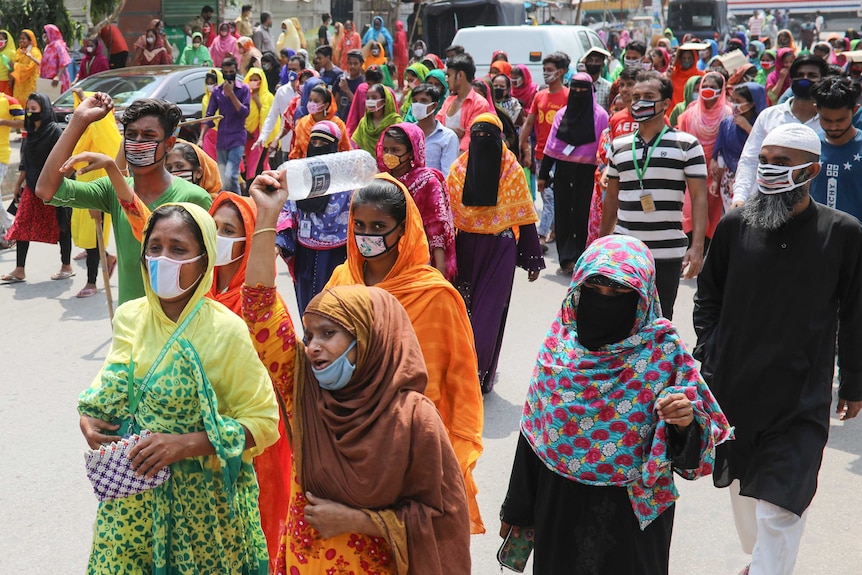 Women and men dressed in all colours and wearing masks march down a street.