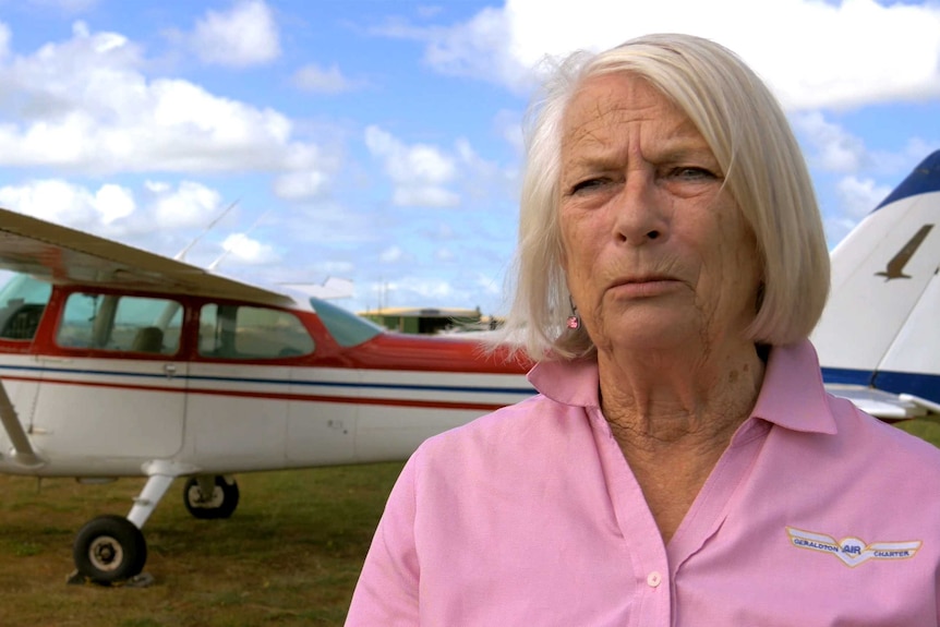 A woman in a pink t-shirt stands next to a red and white light plane.