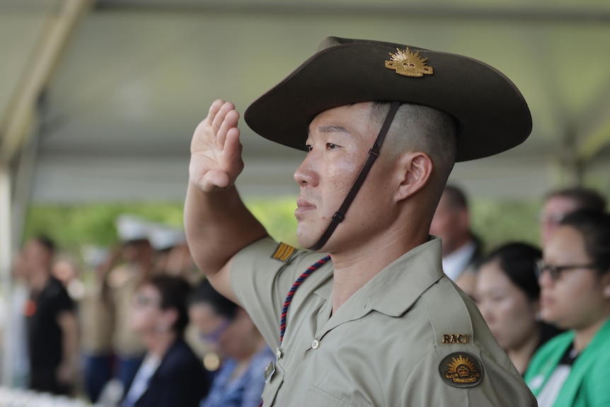 A soldier saluting, amid a crowd of people under a marquee. 