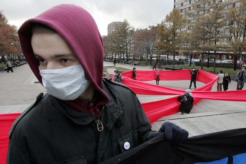 Activists make a large red ribbon, a sign of support for people living with HIV, as another holds a banner during a protest.