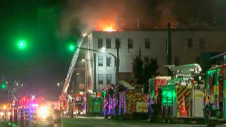 Flames rising out of a building with several firetrucks lined outside. 
