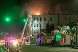 Flames rising out of a building with several firetrucks lined outside. 